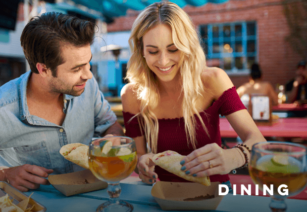 a couple, man and woman, eating tacos with cocktails on the table, with text reading Dining